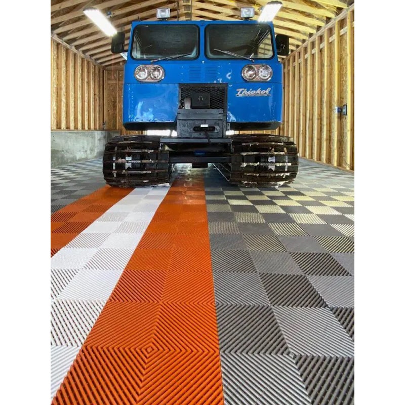Garage featuring RaceDeck Free-Flow XLC Flooring Tiles, showcasing a blue tracked vehicle on a striking orange and gray patterned floor
