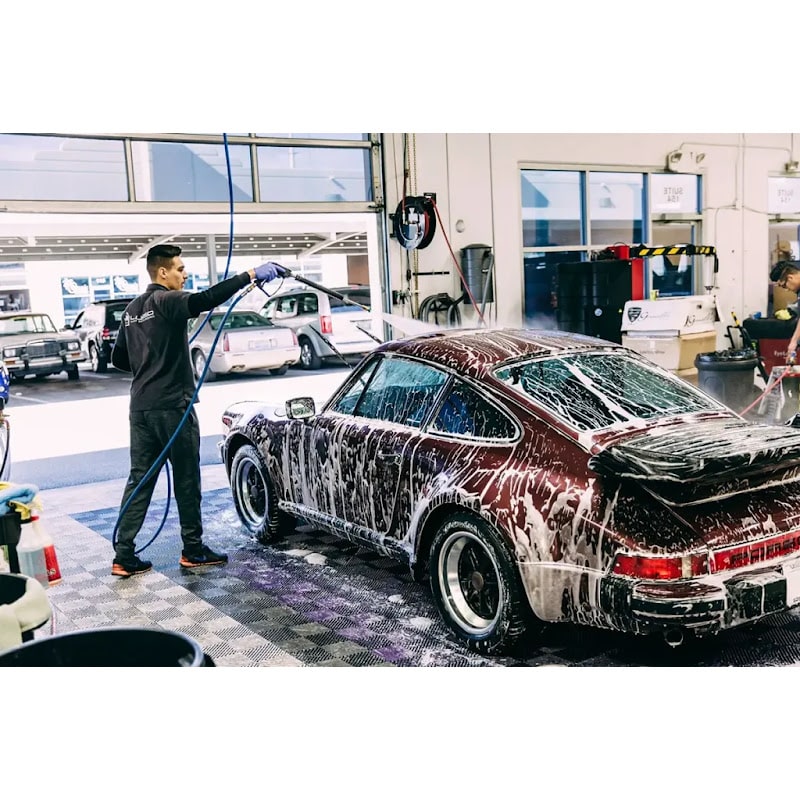 Car wash area featuring RaceDeck Free-Flow XLC tiles, depicting a worker washing a classic Porsche 911 on a stylish checkered floor