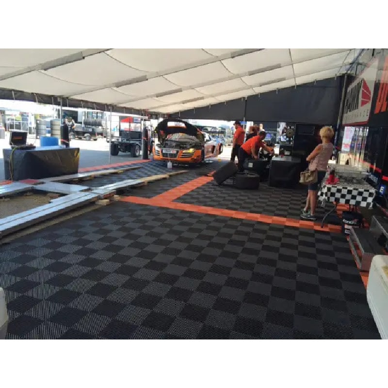 Racing event setup featuring RaceDeck Free-Flow XLC flooring, showcasing a team working in a tent with a car and equipment on a checkered floor