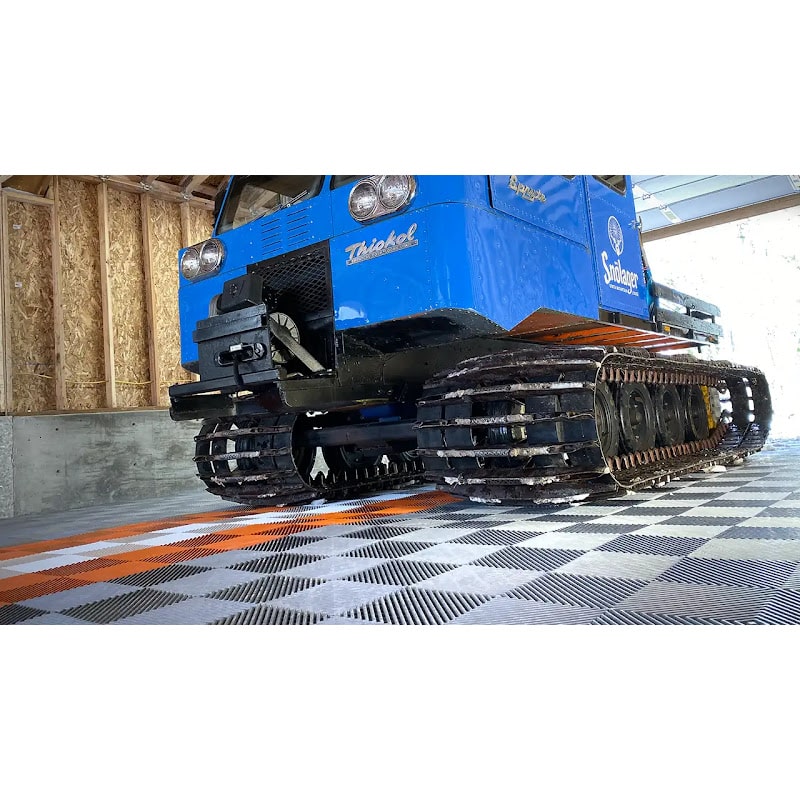 Close-up of a blue tracked vehicle in a garage with RaceDeck Free-Flow XLC flooring, displaying a vibrant orange and gray tile pattern