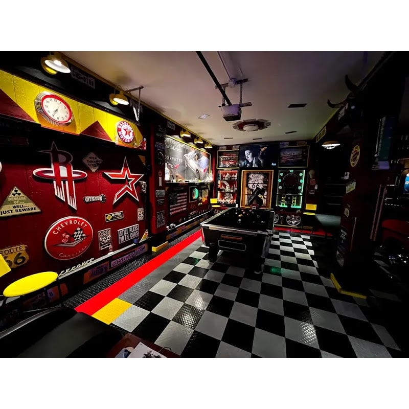 Themed garage with RaceDeck TuffShield tiles, featuring a stylish entertainment area adorned with vintage signs and a bold checkered floor