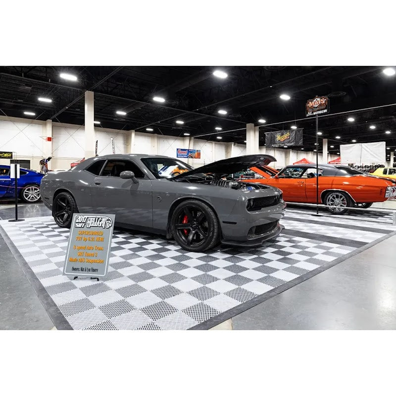 Car show display featuring XLC Race Track Flooring, highlighting a gray muscle car on a clean checkered floor, surrounded by other vehicles